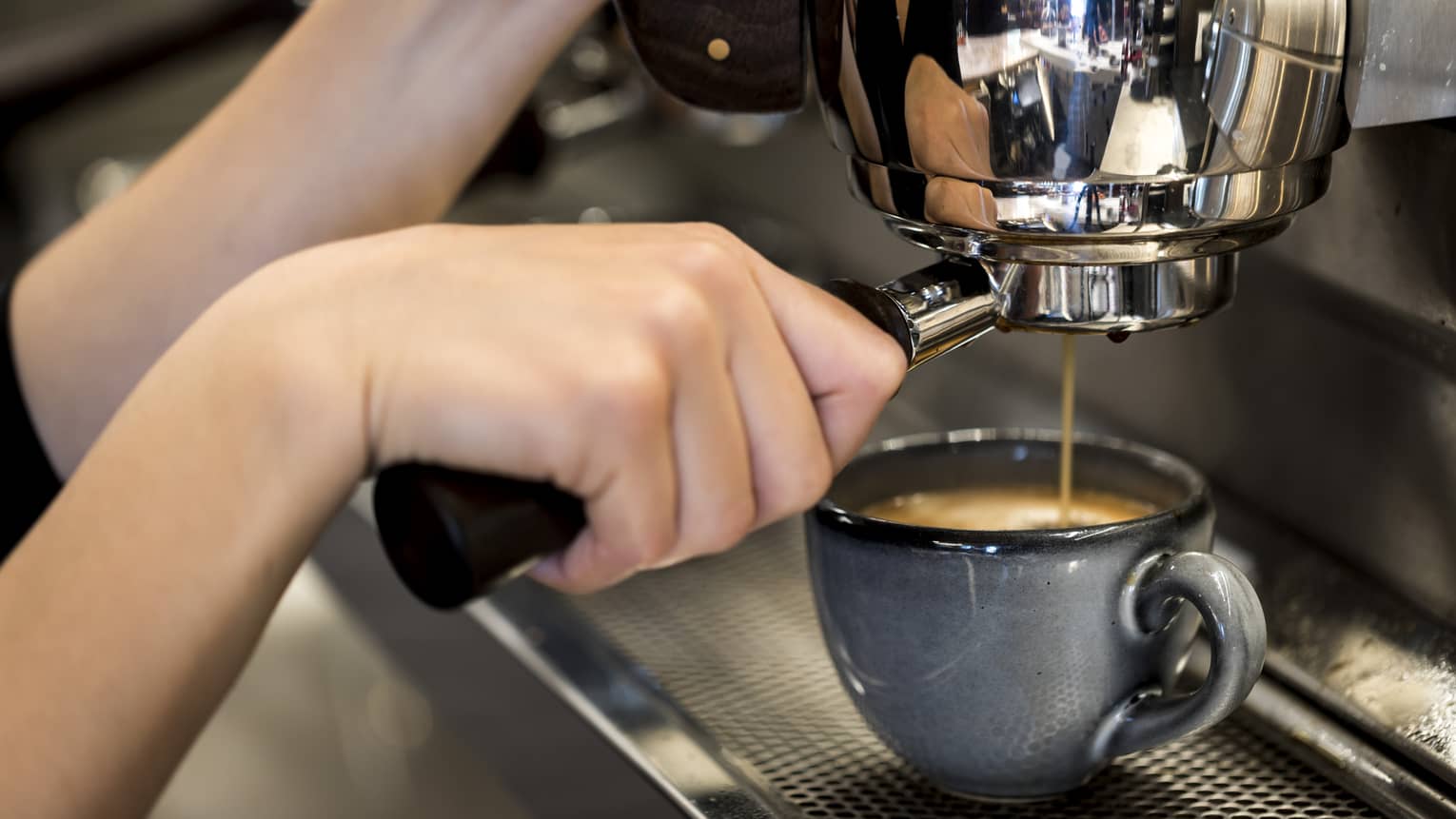 Close-up of hands pressing espresso in machine into small blue mug