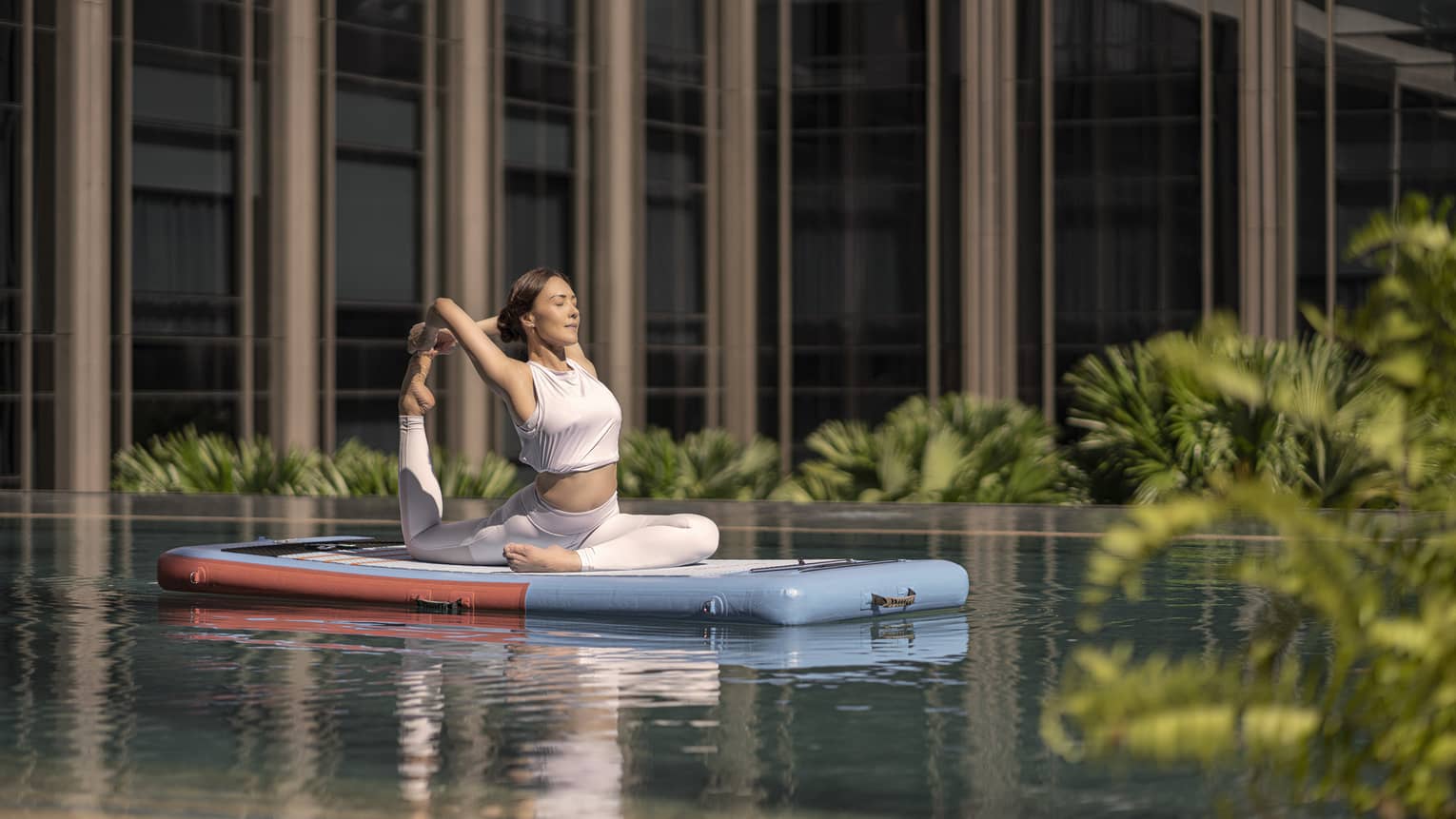 Woman doing a yoga pose on a floating paddle board in hotel pool