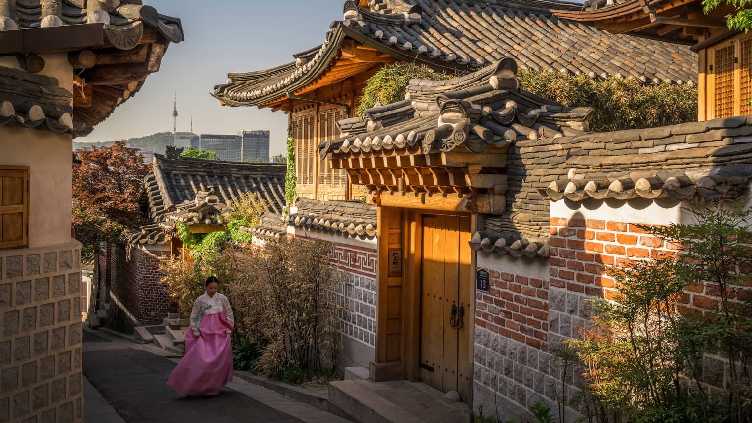 Woman wearing pink Korean robe walks down street past historic temple