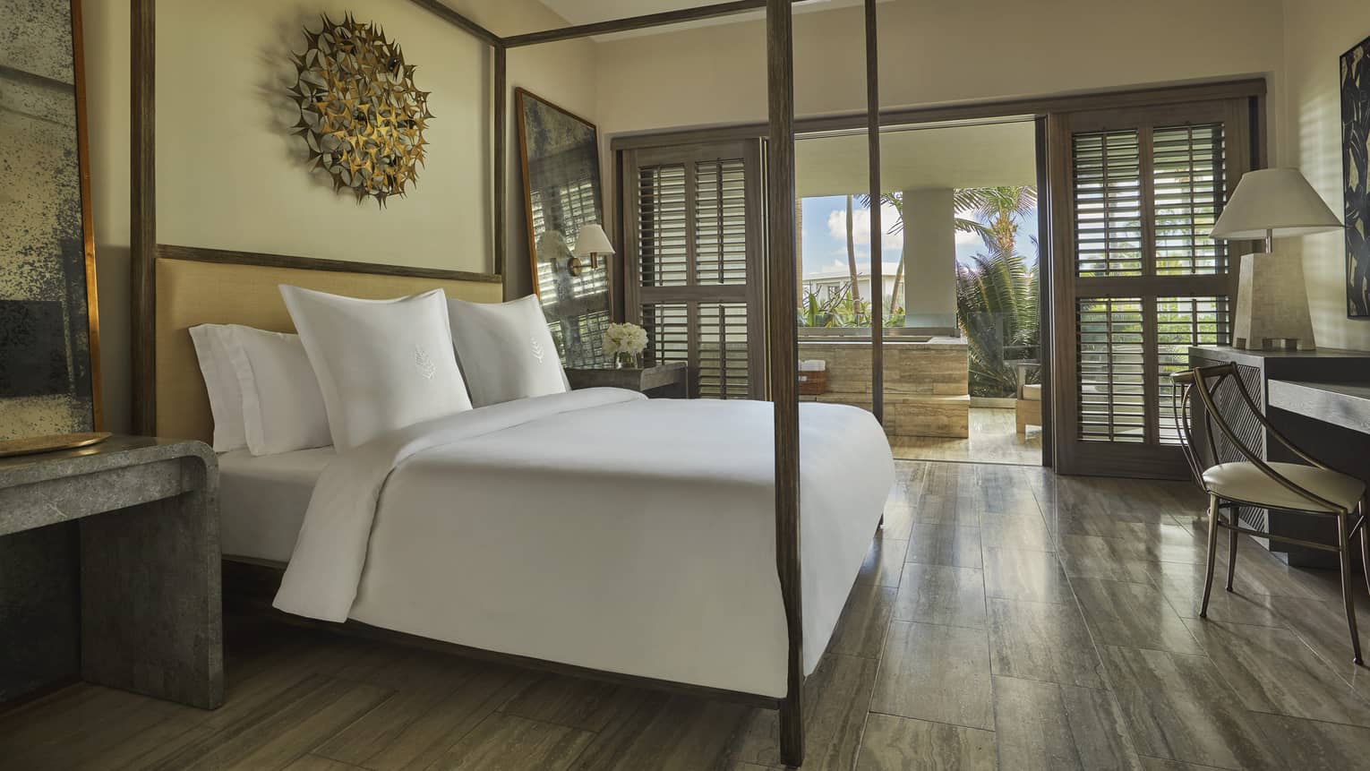 Three-bedroom penthouse bedroom, white bed with canopy frame, brass art on wall, desk, open patio door with wood shutter
