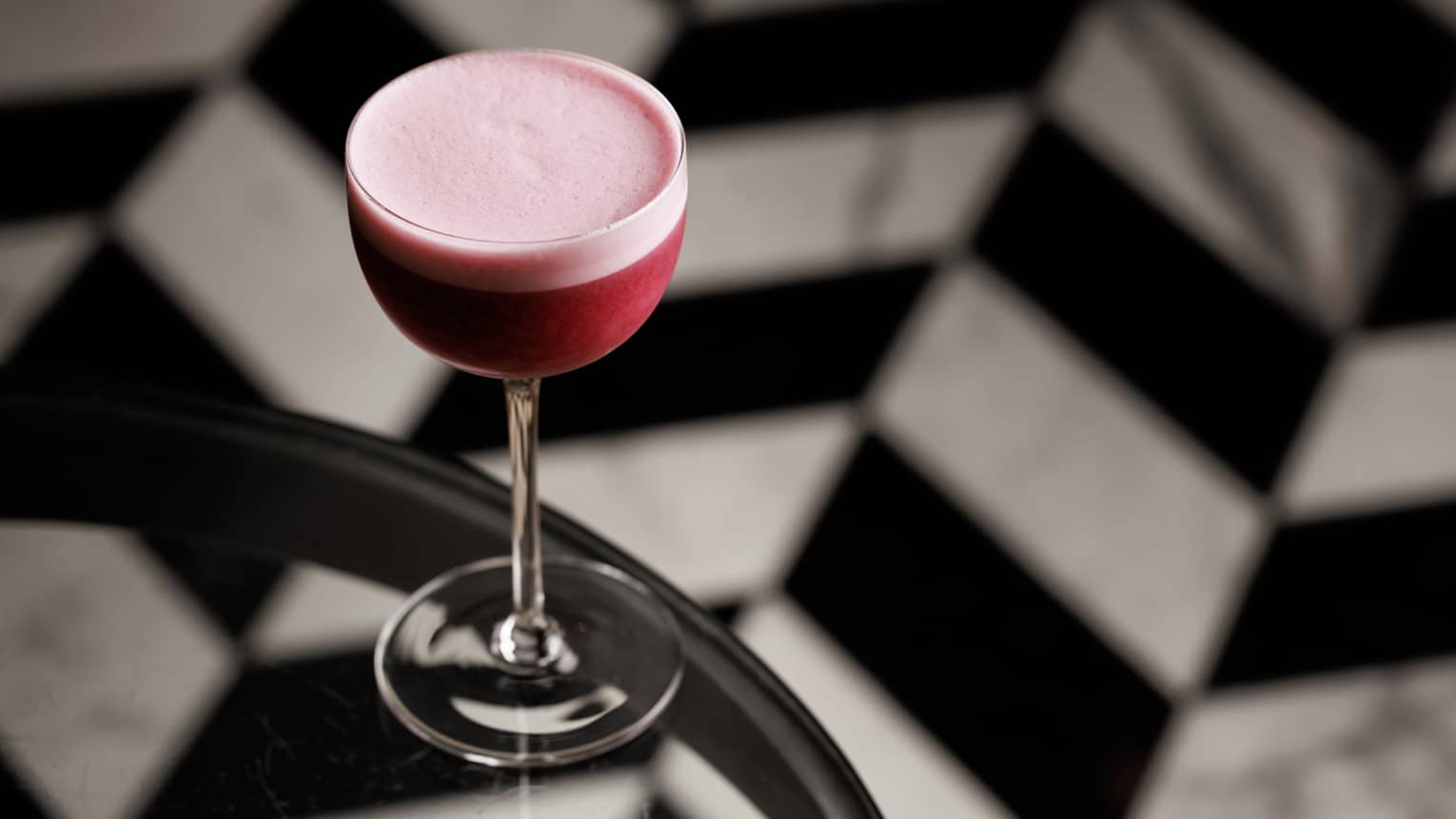 Maroon-coloured cocktail with a pink foam head in a stemmed glass