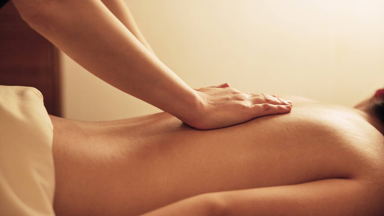 Masseuse rests hands on woman's bare back as she lays on massage table