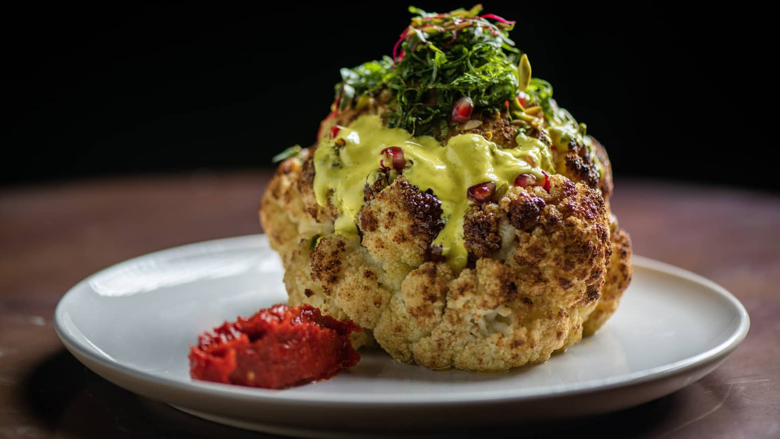 Roasted cauliflower served with turmeric tahini, zaatar, date molasses, pomegranate seeds and pistachio on a round white plate