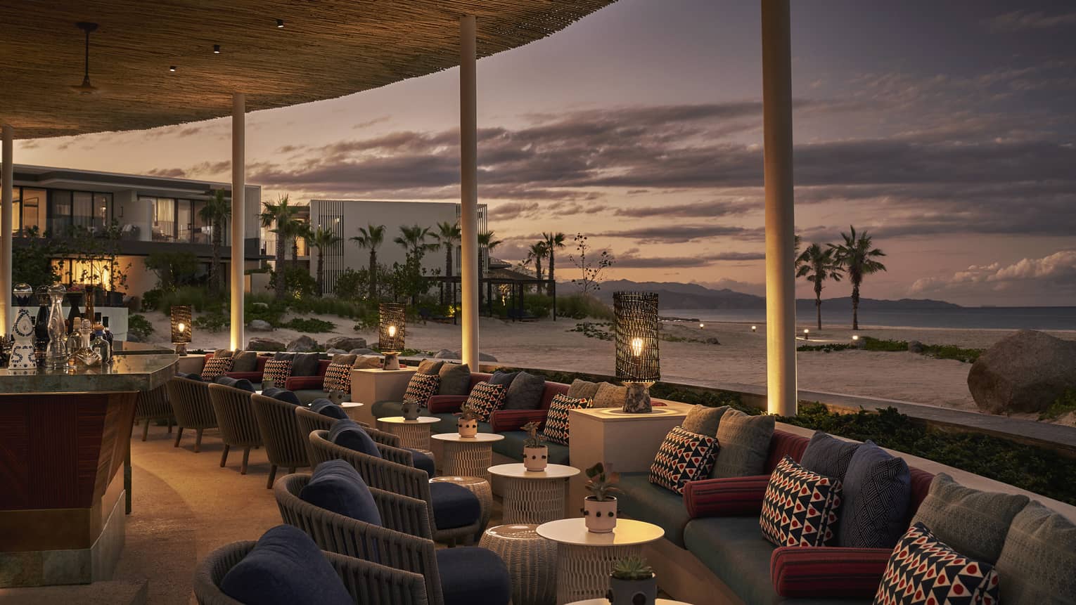 Dimly lit Casa de Brasa lounge area overlooking beach with palm trees at dusk