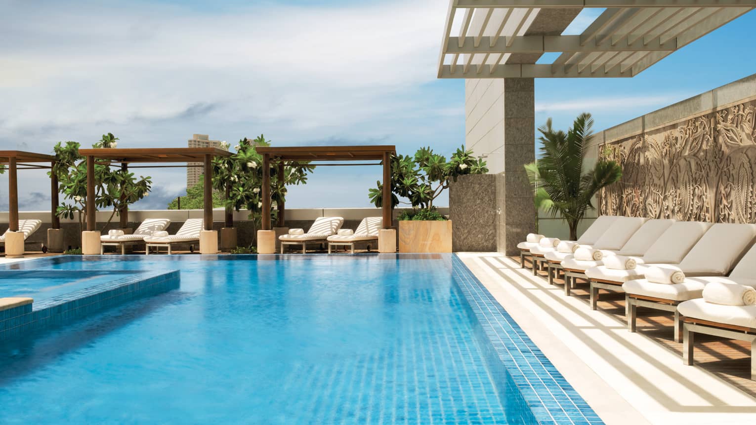 White lounge chairs under pergola by sunny outdoor swimming pool