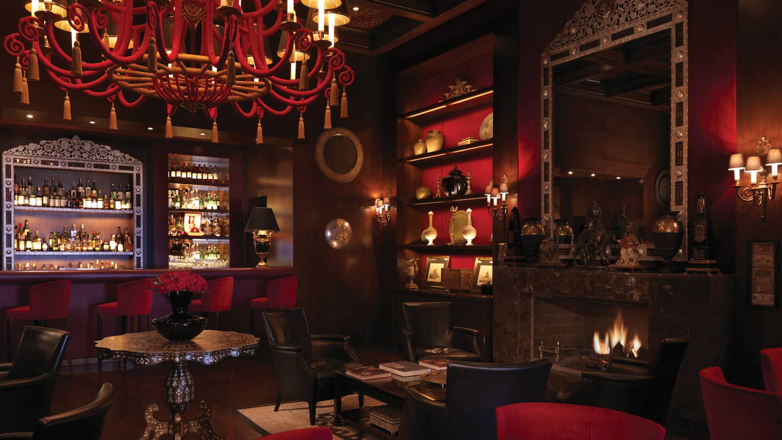 Bar interior with dark wood, red chandelier, shelf and velvet bar stools, arabesque ceiling, fireplace