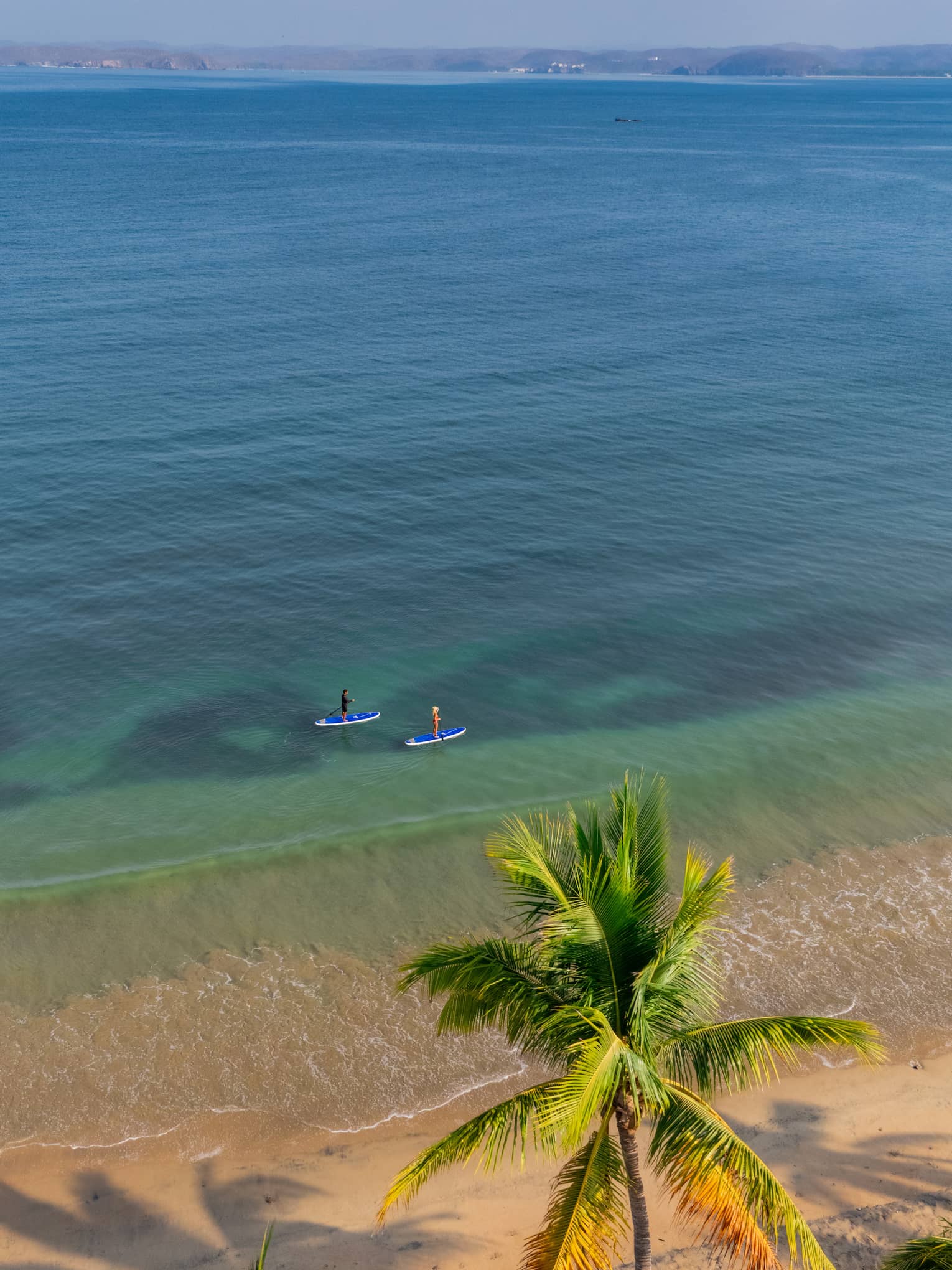 Two people paddleboarding in clear blue waters along the beach shoreline