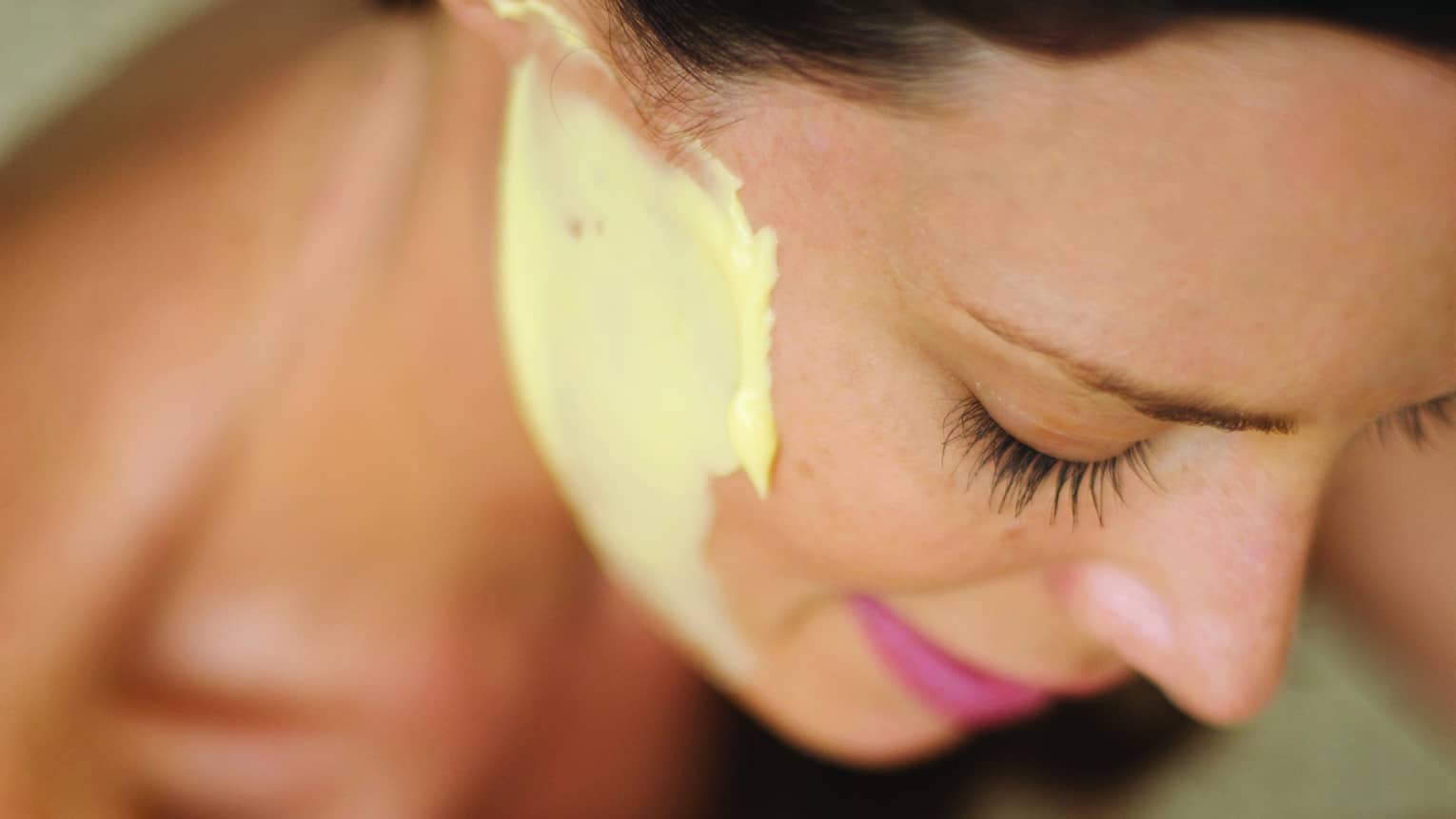 A close up of a woman looking down and smiling, with a yellow Sodashi Facial on her face