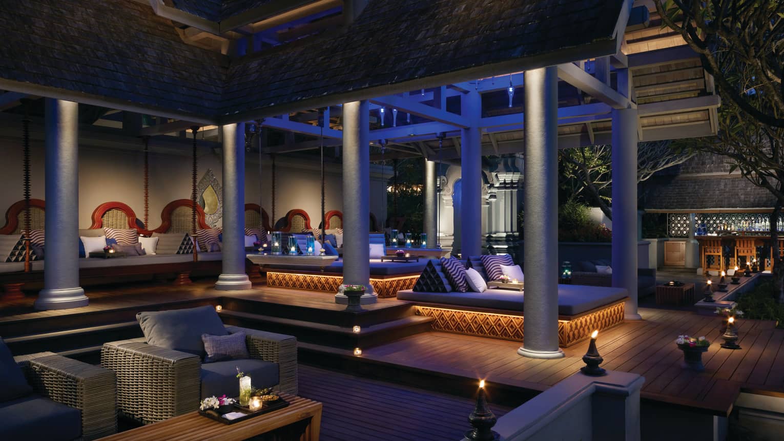 Ratree patio large wicker lounge sofas, chairs, small lanterns under white pillars at night