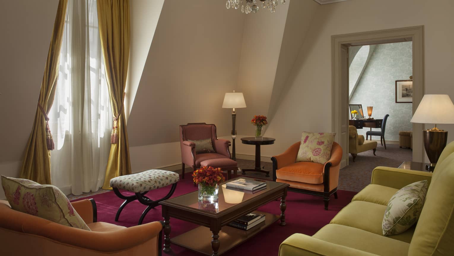 La Mansión Ambassador Suite with pink and orange velvet armchairs, yellow sofa under sloped walls, small crystal chandelier