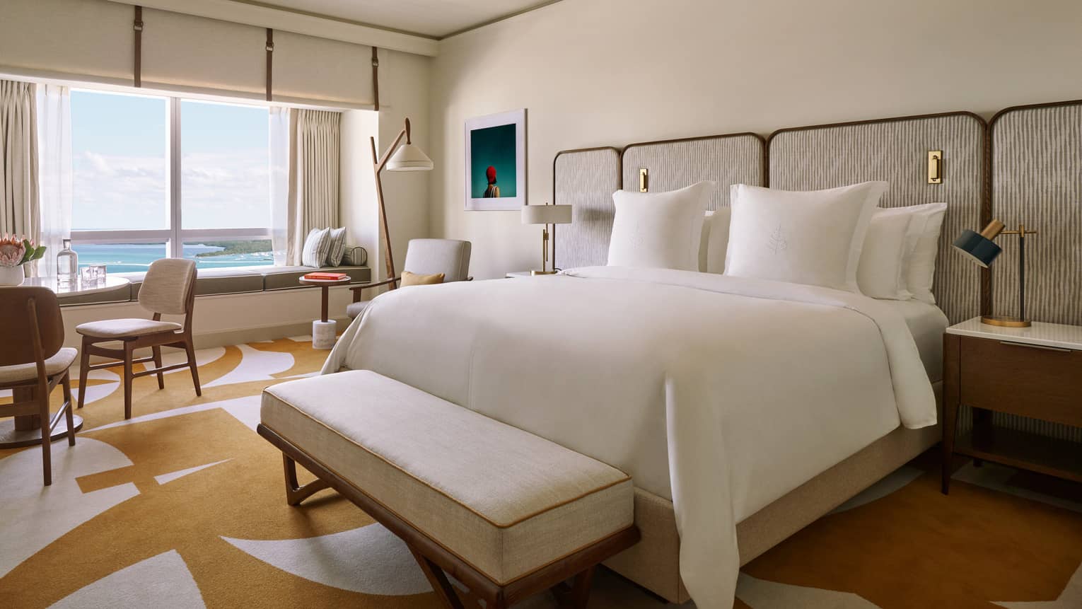 Room with a bed, table, chairs, and a window with a window seat and view of the ocean.