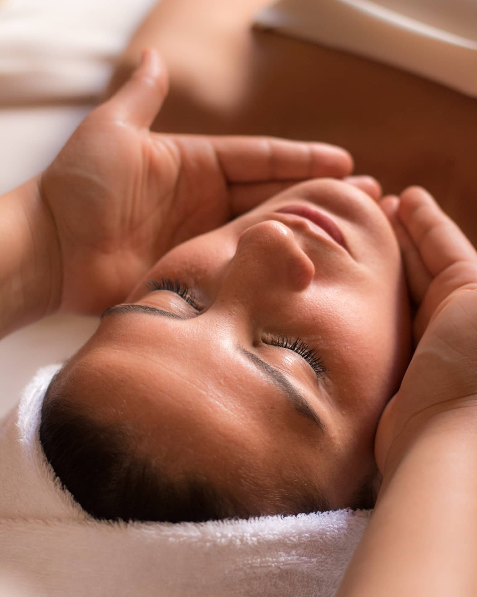 Close-up of woman with eyes closed facing up as hands cup her face and chin