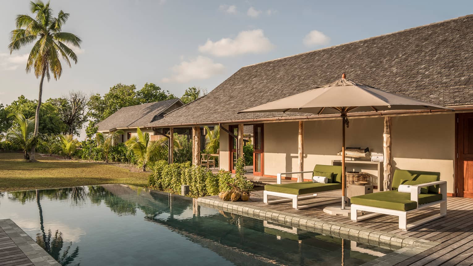 Palm tree reflecting on plunge pool under bungalow small patio with two lounge chairs, umbrella