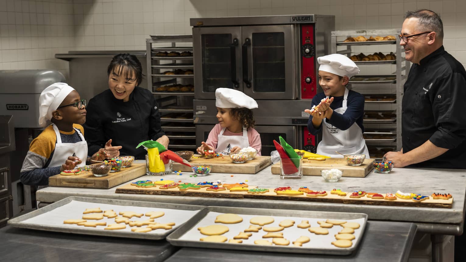 Three children and two chefs making cookies.