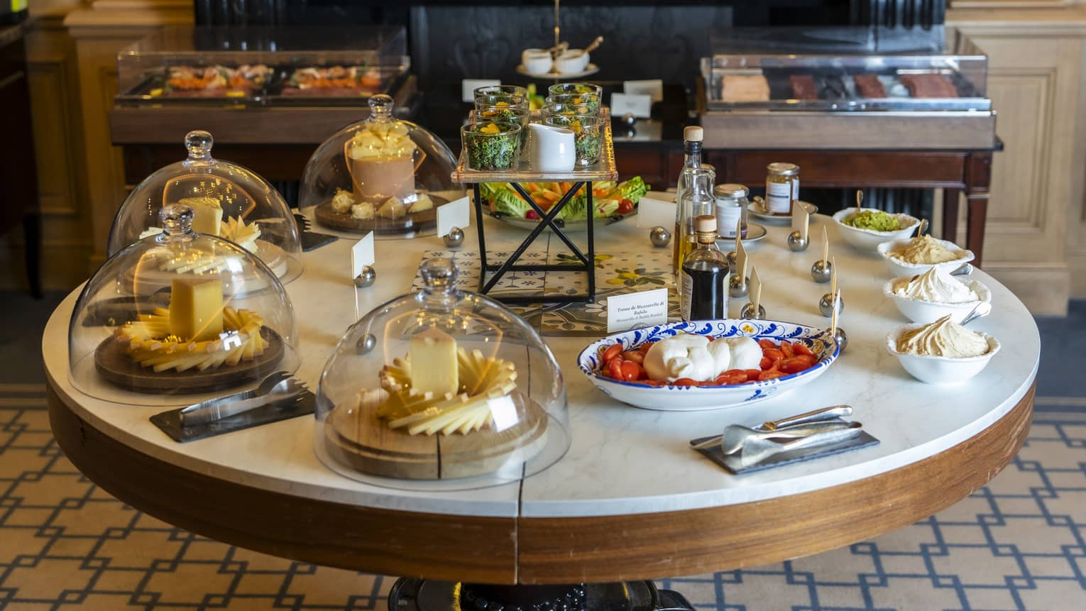 A round dining table set with a spread of plated breakfast food items, some of which are under glass domes.