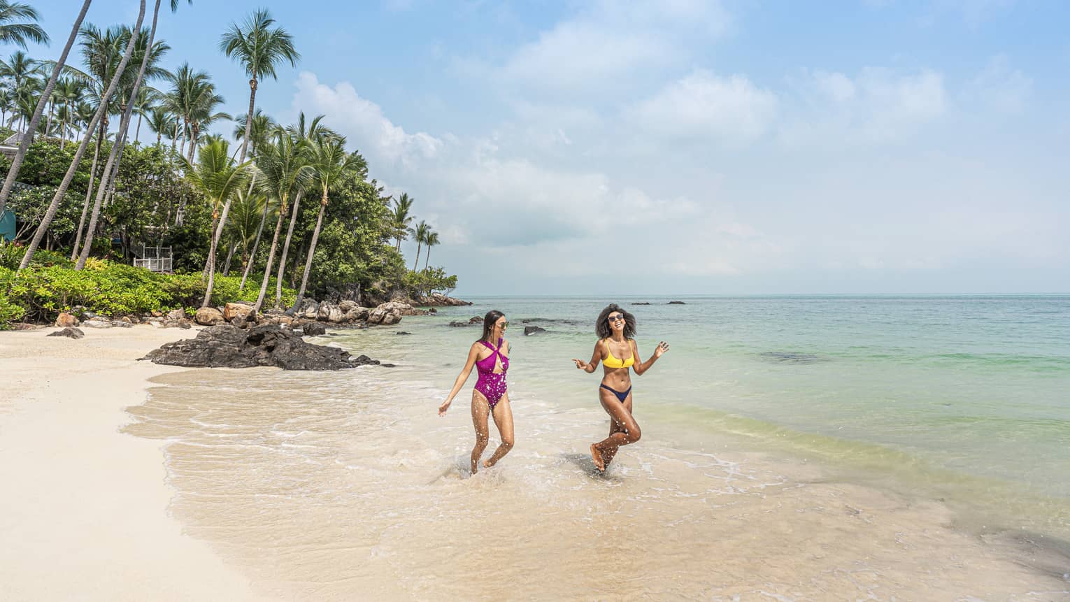 Two women in bathing suits laugh and frolic on the shore