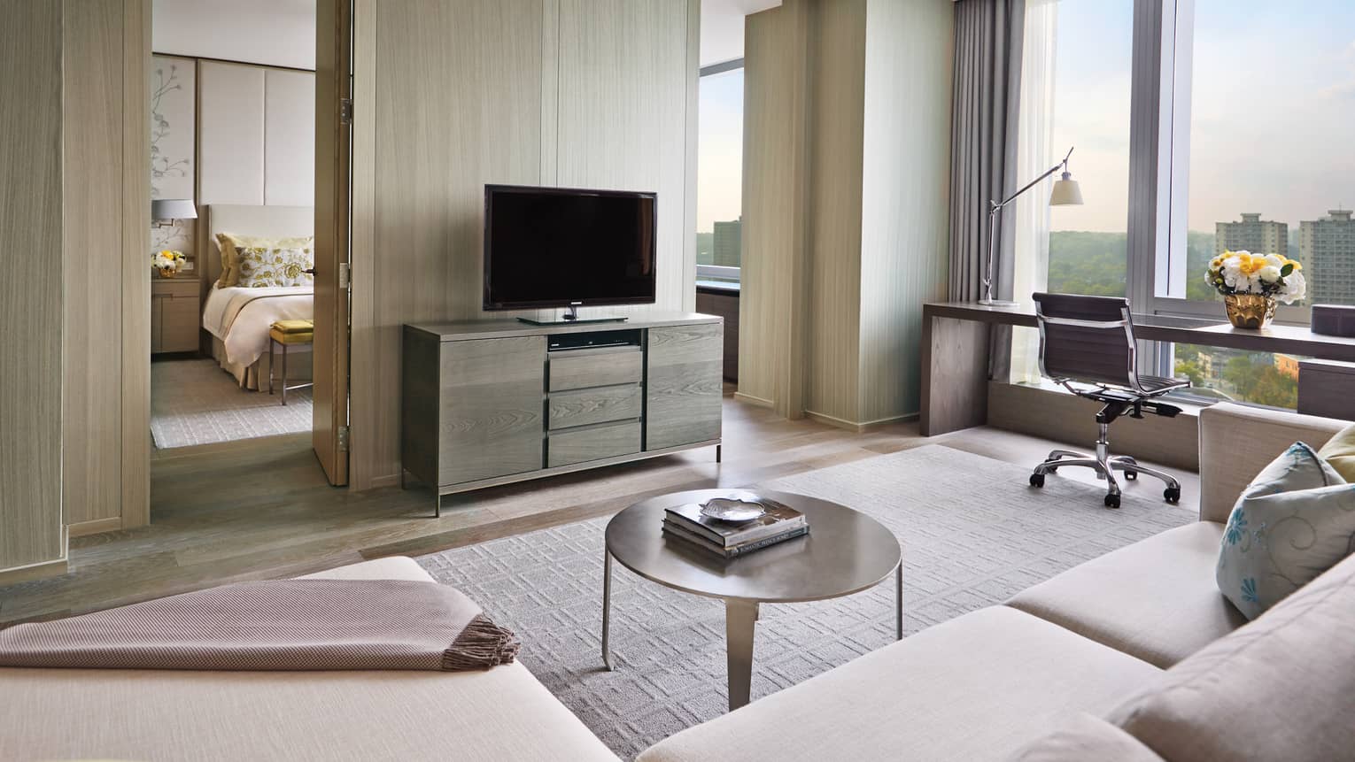 Bright, modern hotel suite, TV against birch wood wall to bedroom, desk by floor-to-ceiling window