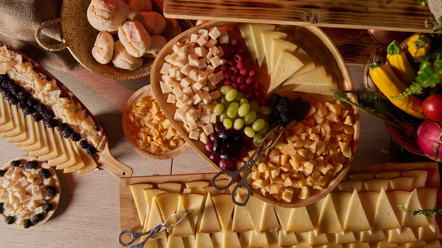 Large display of triangle-shaped cheese slices, grapes, berries, dried fruit and a basket of bread rolls