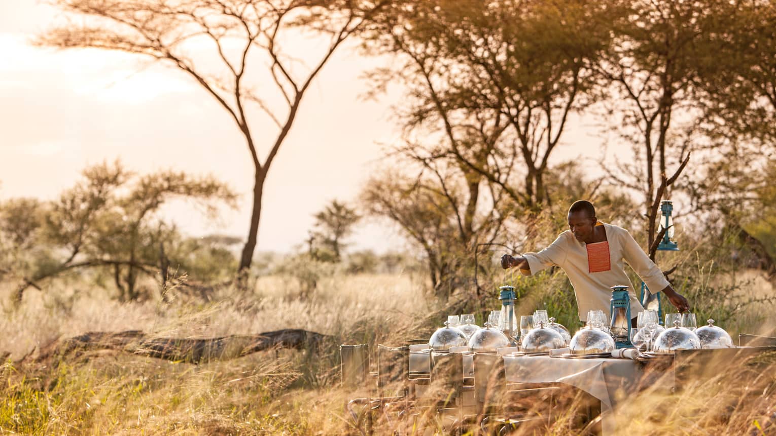 Hotel staff places lantern on long dining table with silver dome planets in grassy field