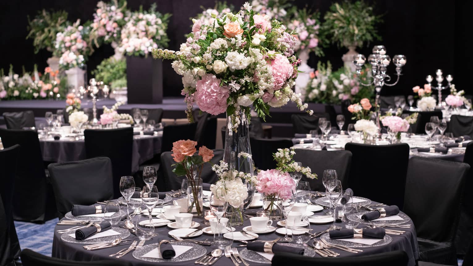 A wedding reception set up with round tables, all-black linens and tall floral centerpieces of white, pink and peach flowers