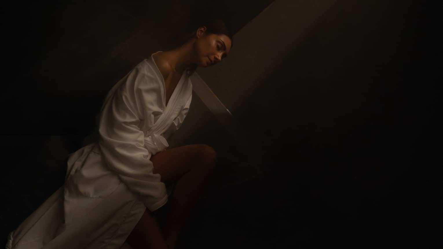 Guest wearing white robe sits in a dimly lit eucalyptus-infused steam room