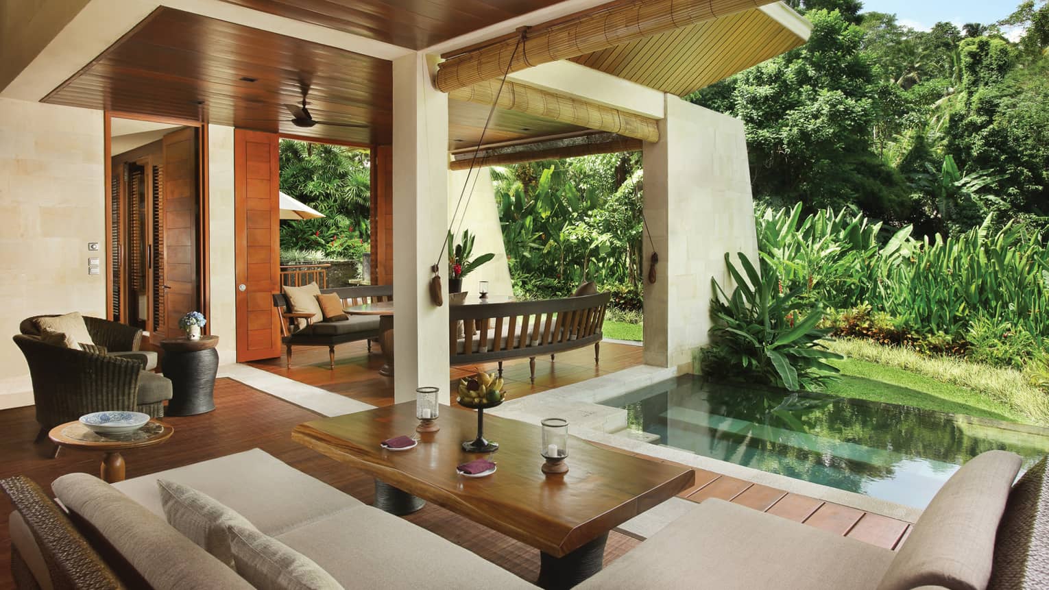 Two Bedroom Villa open-air living space with wood floors, white patio sofa, plunge pool beside green tropical plants