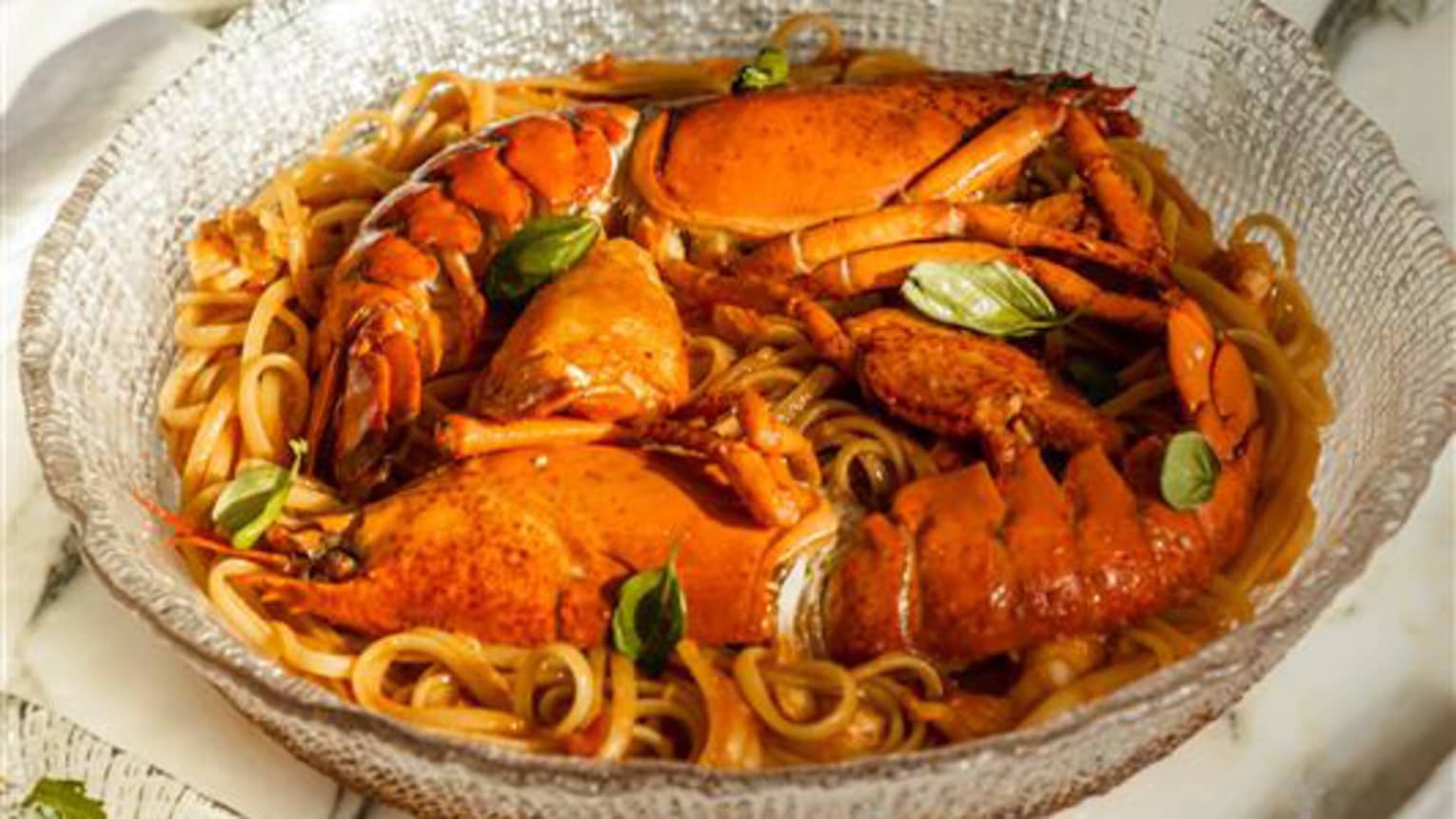 Lobster linguine served in a shallow glass bowl atop a white marble table