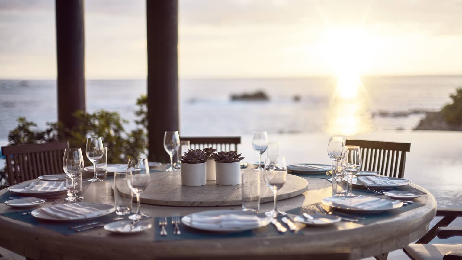 Round outdoor dining table with wine glasses, ocean and sunset in background