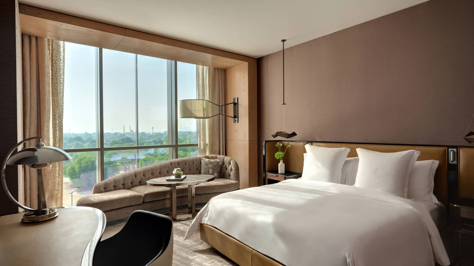 Bedroom with brown walls, white king bed, desk and chaise by the window