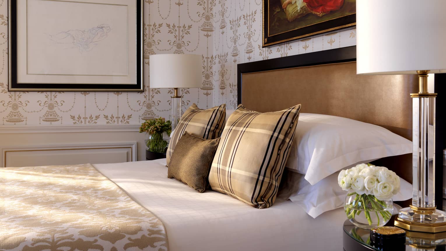 Close-up of bed with brown-and-gold plaid accent pillows, blanket, wallpaper, brown padded headboard