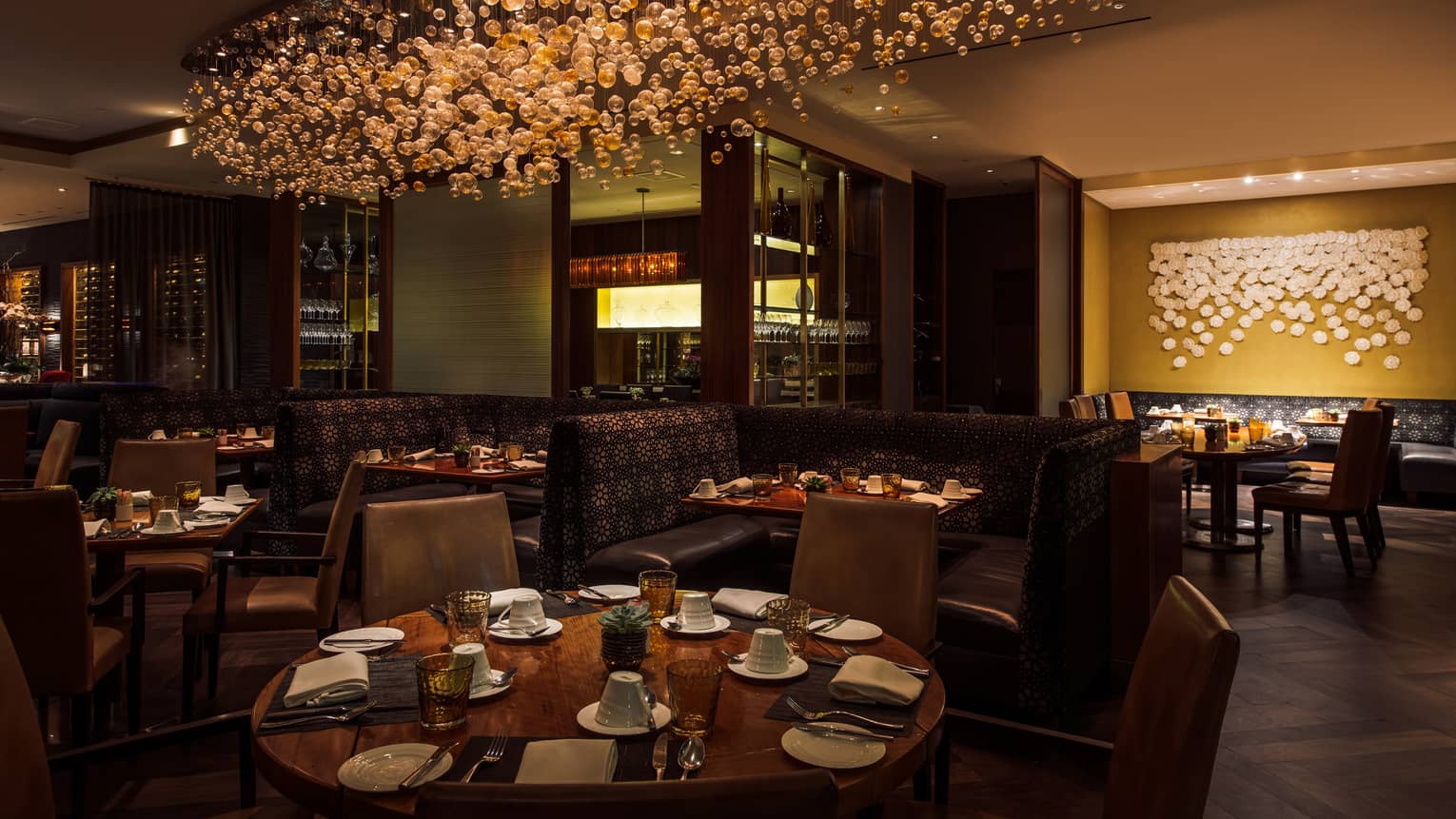 Culina Restaurant round dining tables, booths under modern glass bulb chandelier