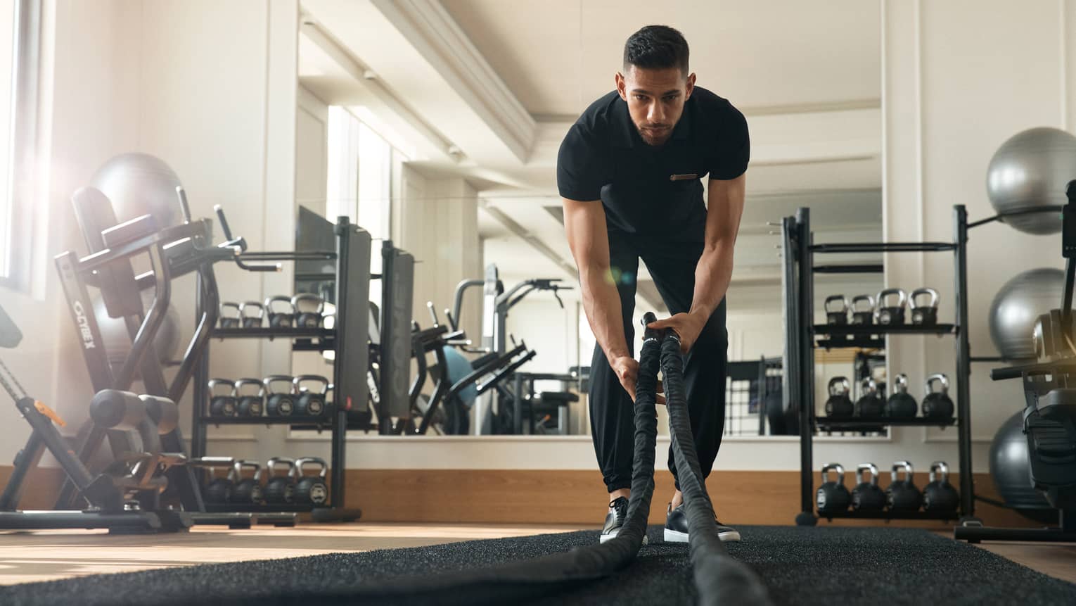 Man works out in fitness room using a heavy rope
