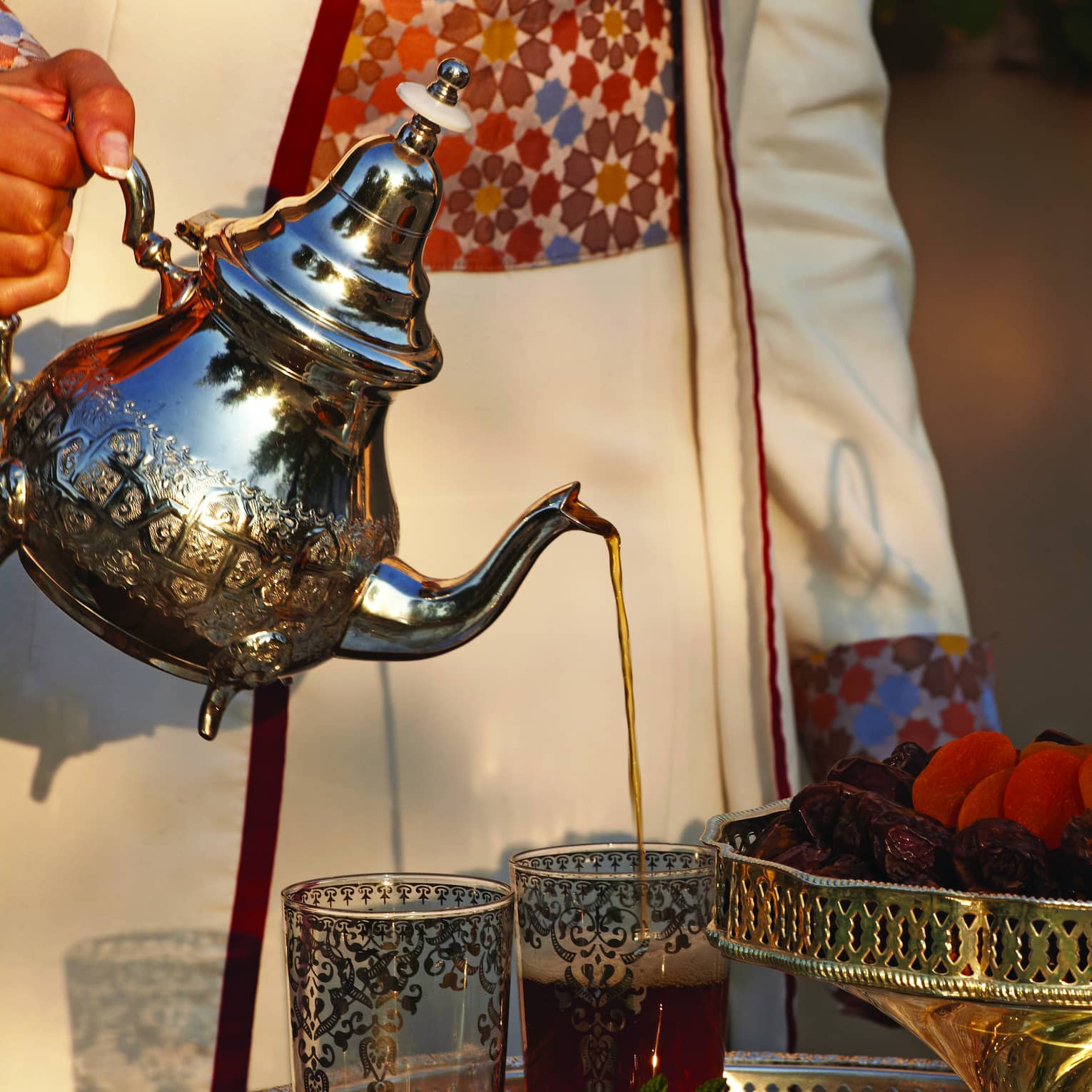 Small silver teapot pouring tea into decorative Moroccan glasses