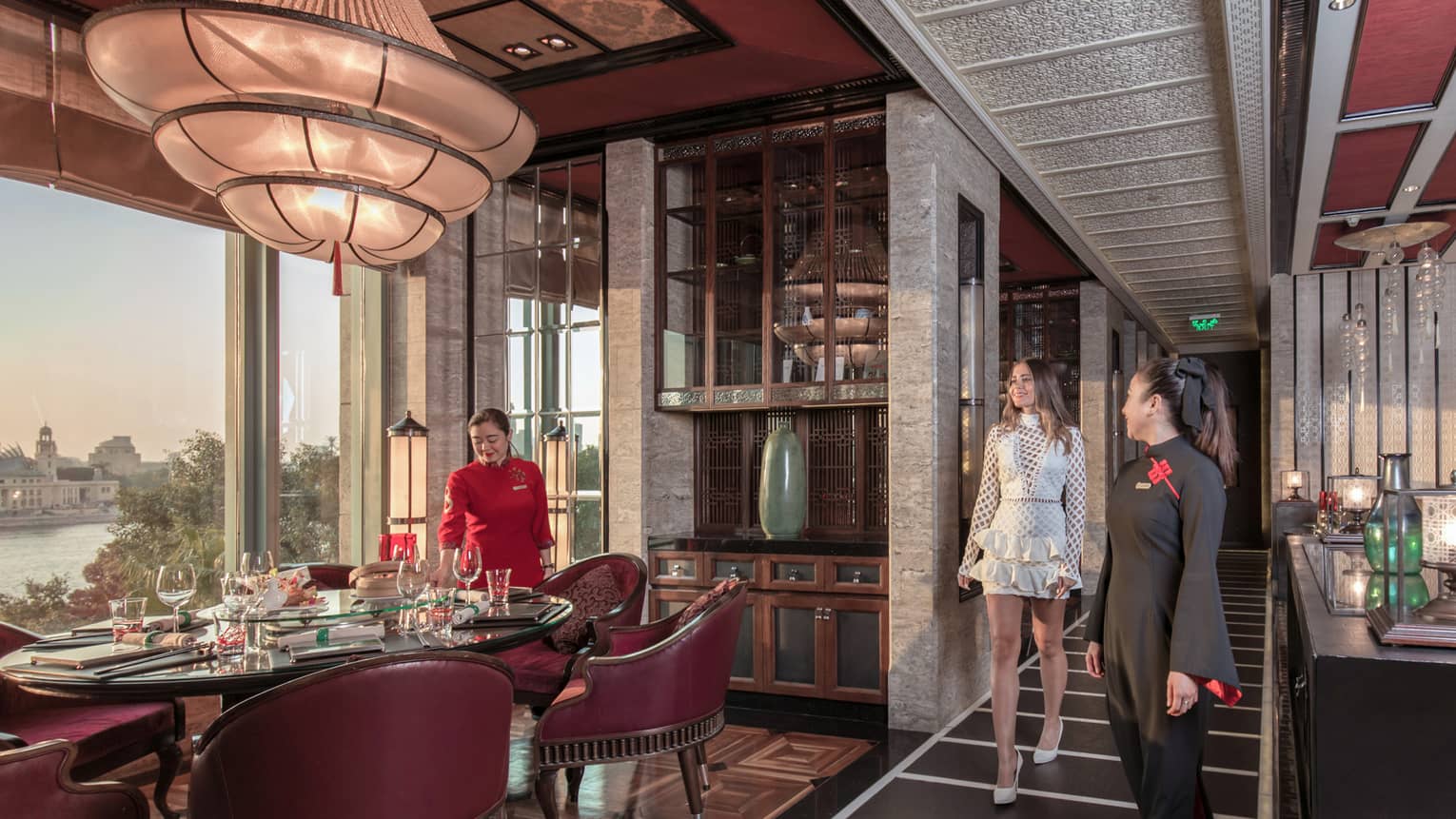 A guest is shown to her table, surrounded by burgundy chairs, in a luxurious restaurant with opulent decorations. 