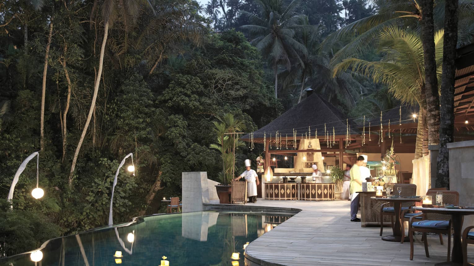 An infinity pool looking out towards the dense jungle; chefs bustle around the outdoor kitchen on the poolside deck.