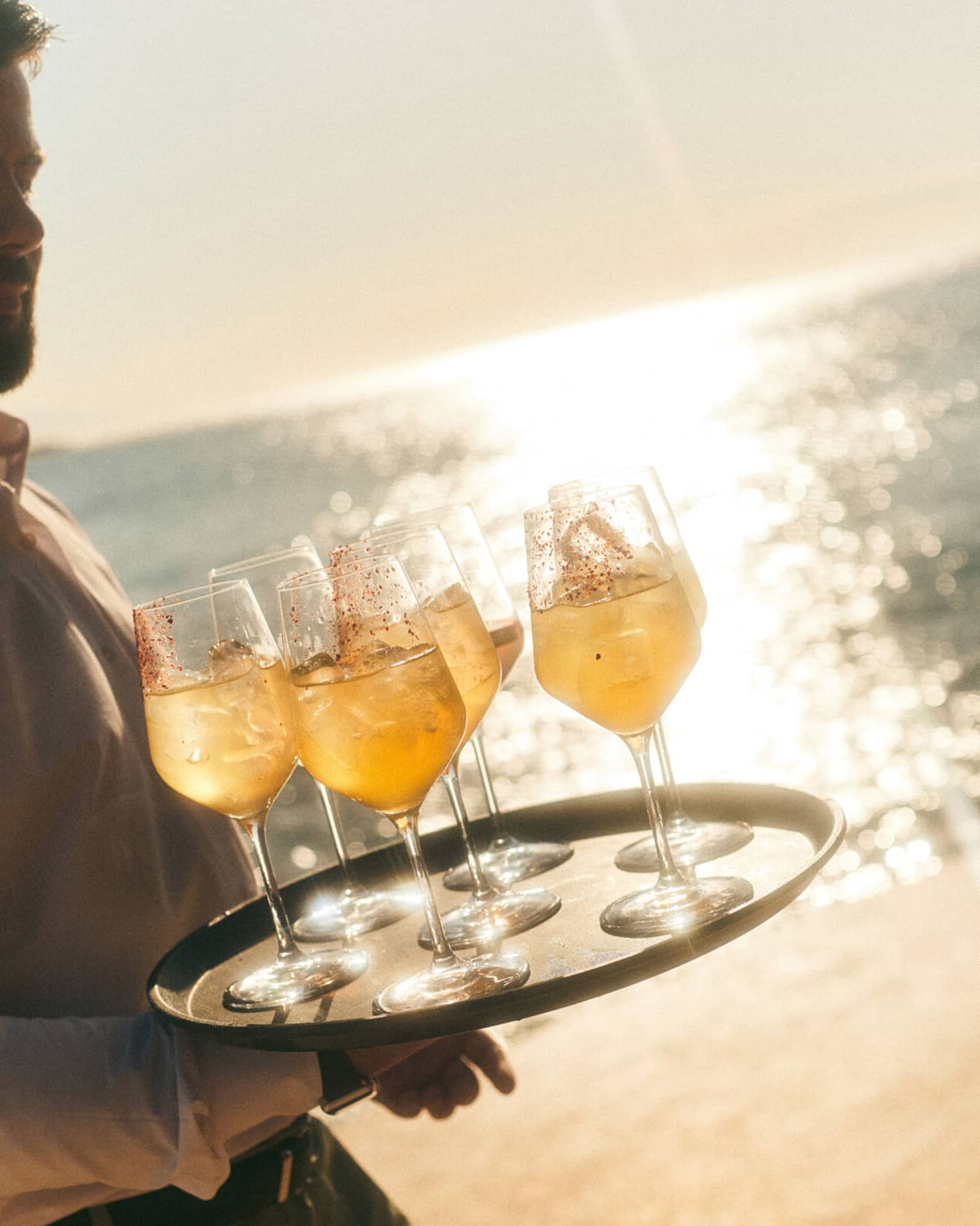 A server holds a tray of orange cocktails on a sunny beach