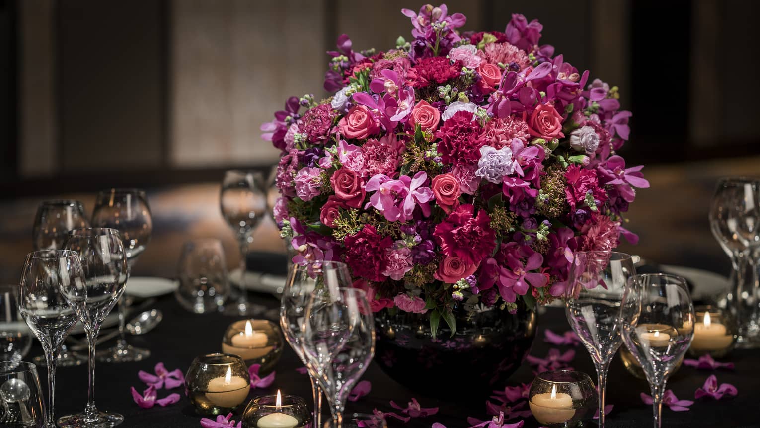 Large vase of colourful flowers on centre of table surrounded by wine glasses and candles