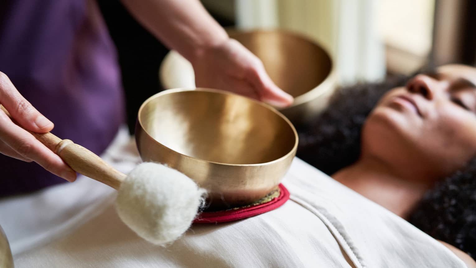 A woman with a sheet on her and a spa team member holding a golden bowl over her.