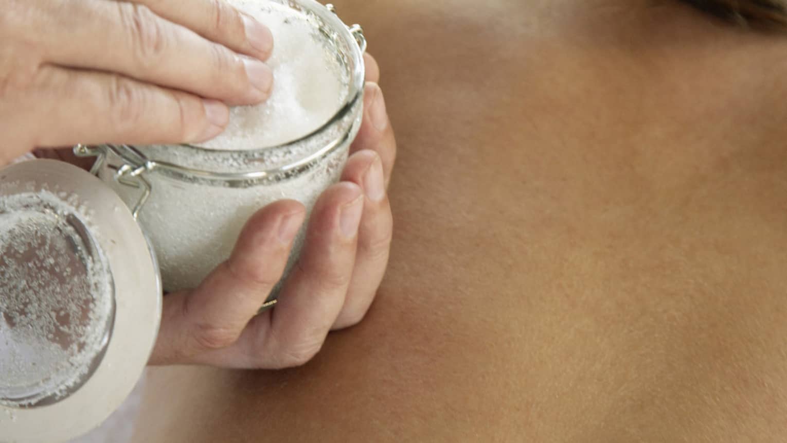 Jar of sea salt scrub above woman's bare back in spa
