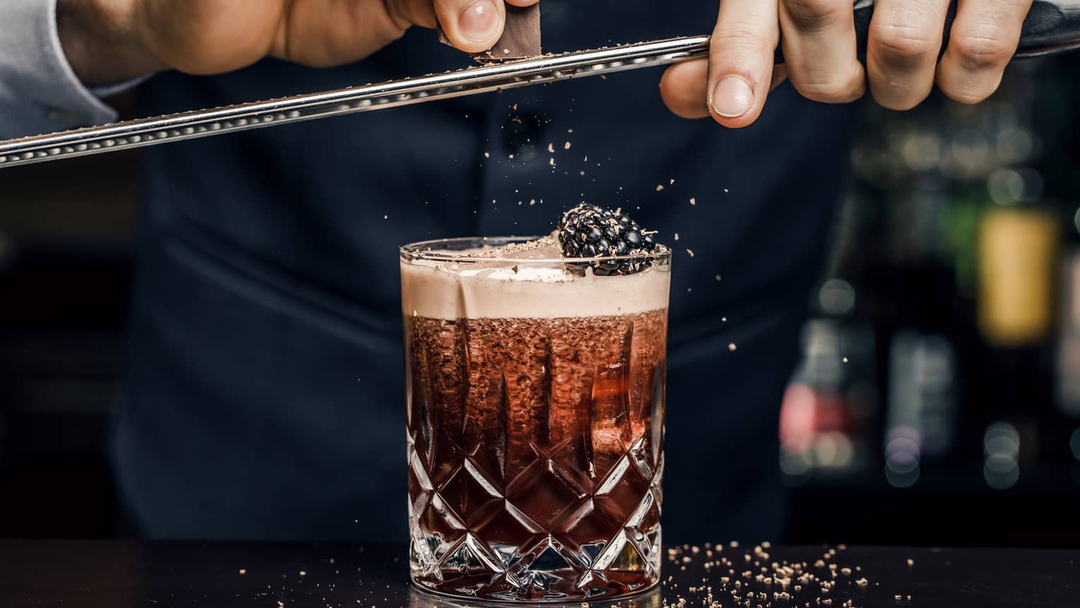 Churchill Club bartender shaves garnish over cocktail in crystal rock glass with blackberry