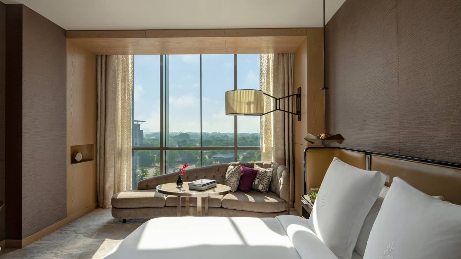 Bedroom with brown walls, white king bed, chaise by the window