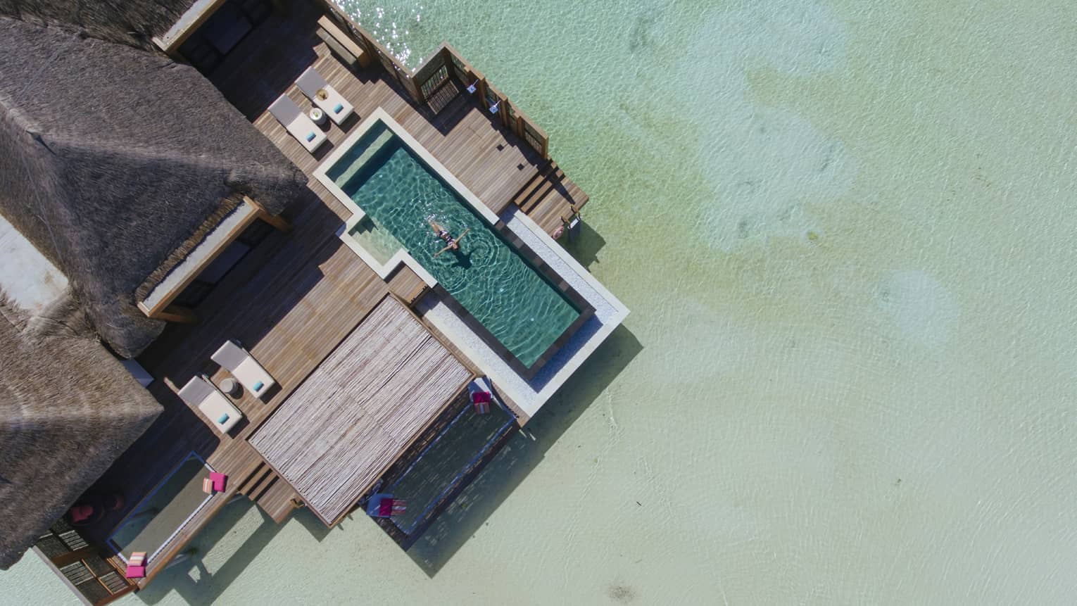 Aerial view of water suite, woman floats on back in private pool