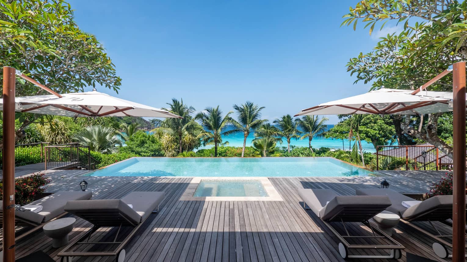 Private pool deck with lounge chairs and umbrellas, facing a pool and the turquoise sea
