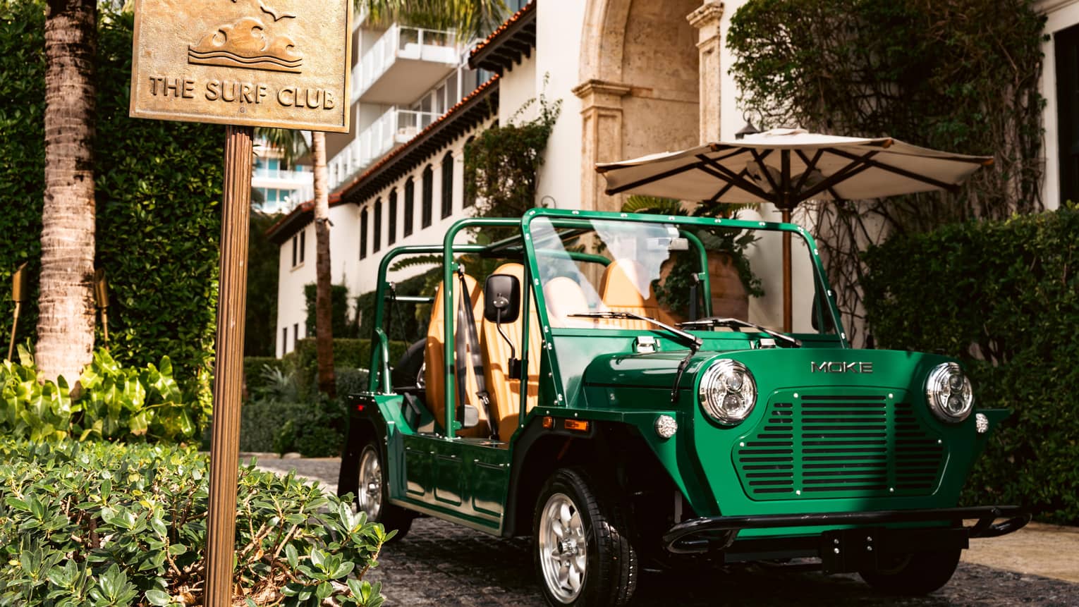 Green MOKE car parked outside of the building next to "The Surf Club" sign.