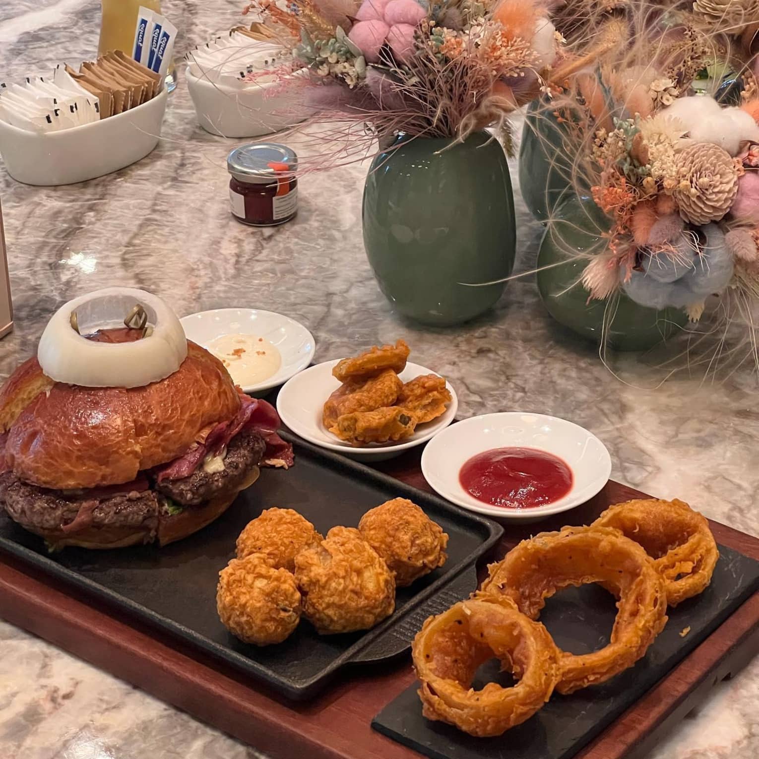 A burger and beer are served at a table decorated with floral arrangements