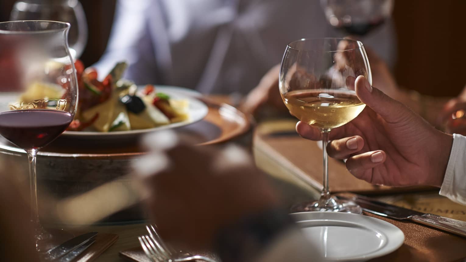 Close-up of hand holding wine glass by dinner plate on table