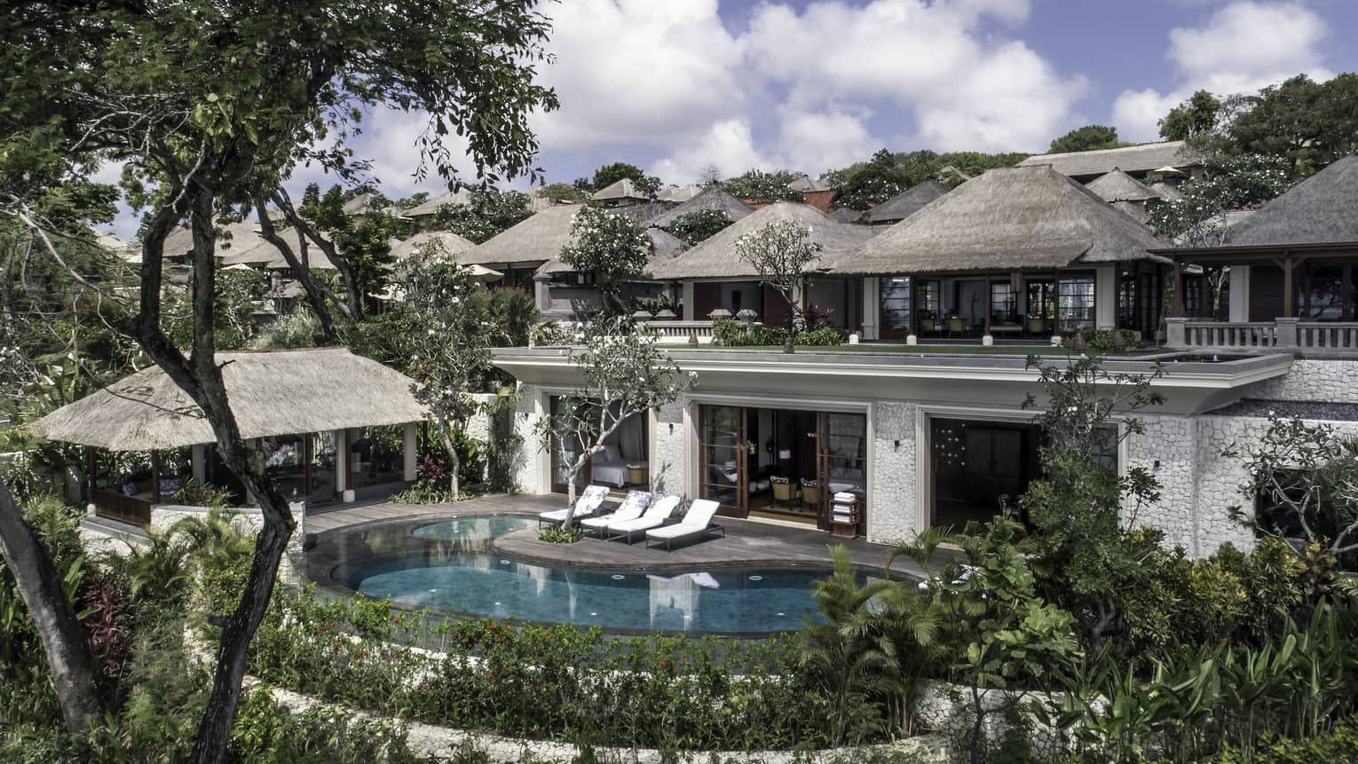 Imperial Villa exterior, looking in from garden at swimming pools, patio, open doors to first storey, thatched roofs on second