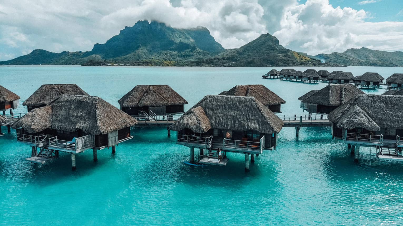 Thatched-roof overwater bungalows at Four Seasons Resort Bora Bora, with mountains in background
