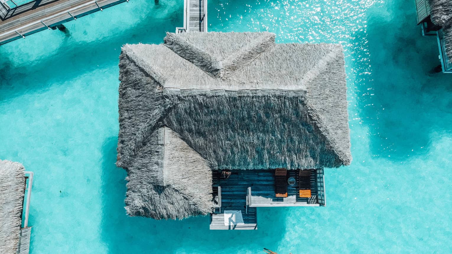 Aerial view of person swimming away from overwater bungalow in turquoise lagoon