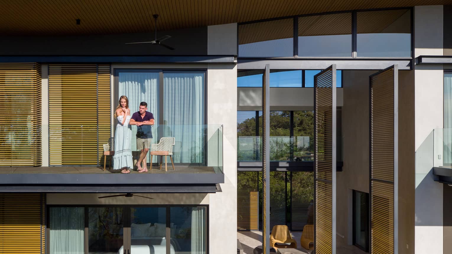 Man and woman stand on glass balcony of villa
